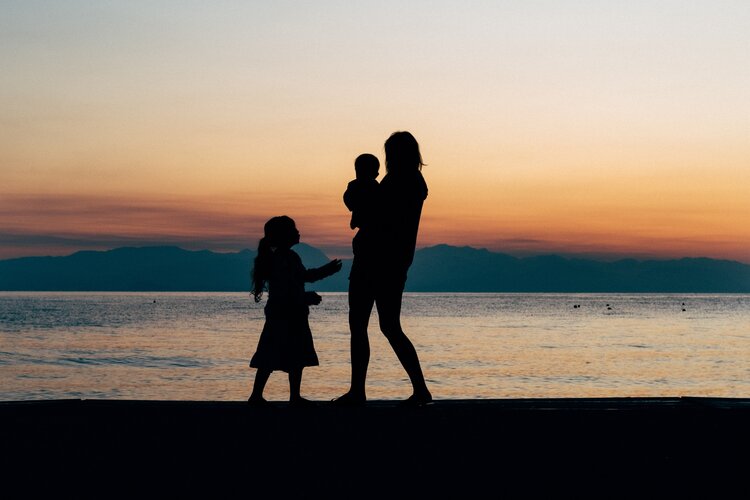 Person stands with two children in front of a beach at sunset